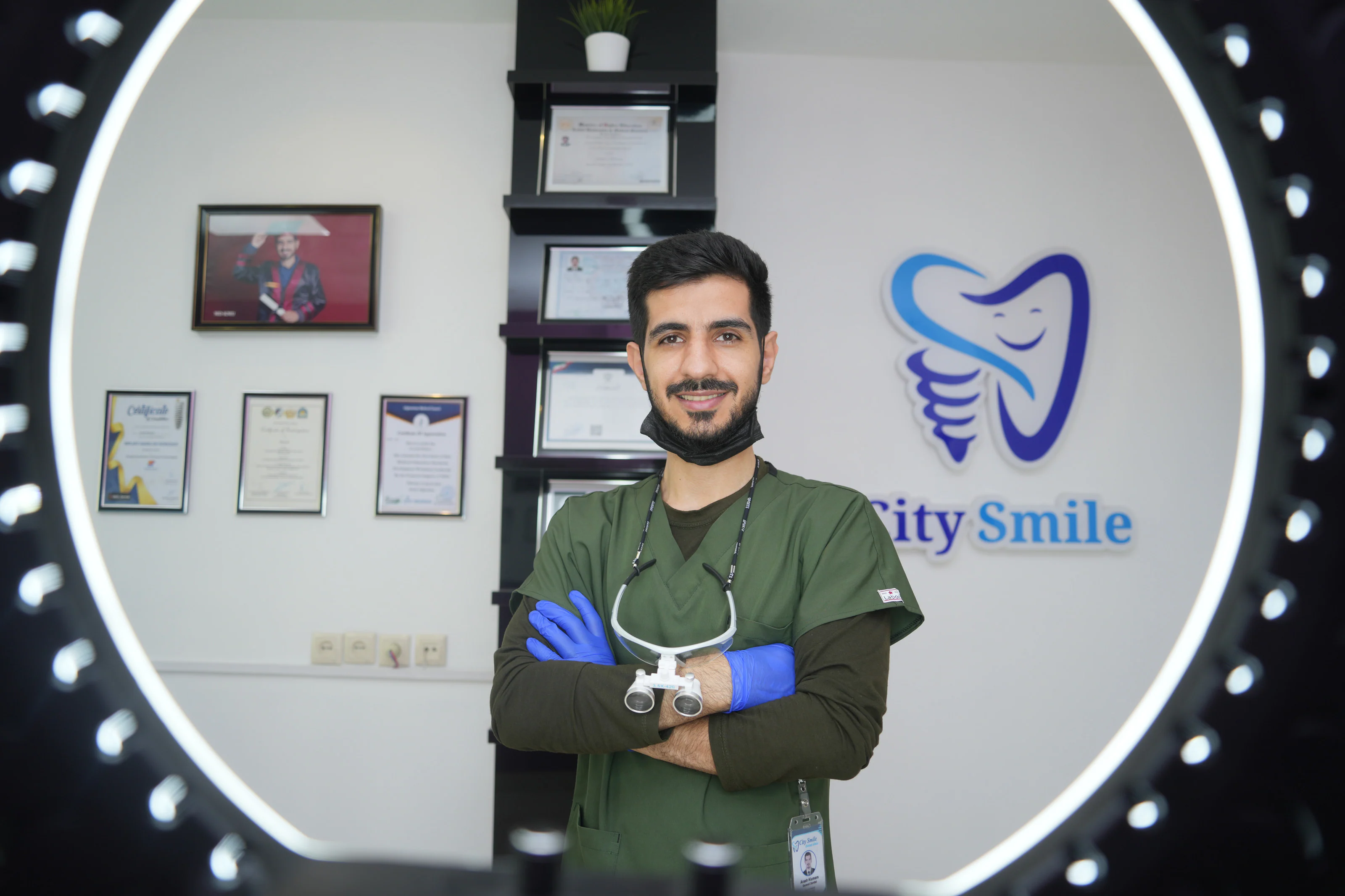 Dr. Arash Kiumars with arms crossed in the clinic, wearing loupes