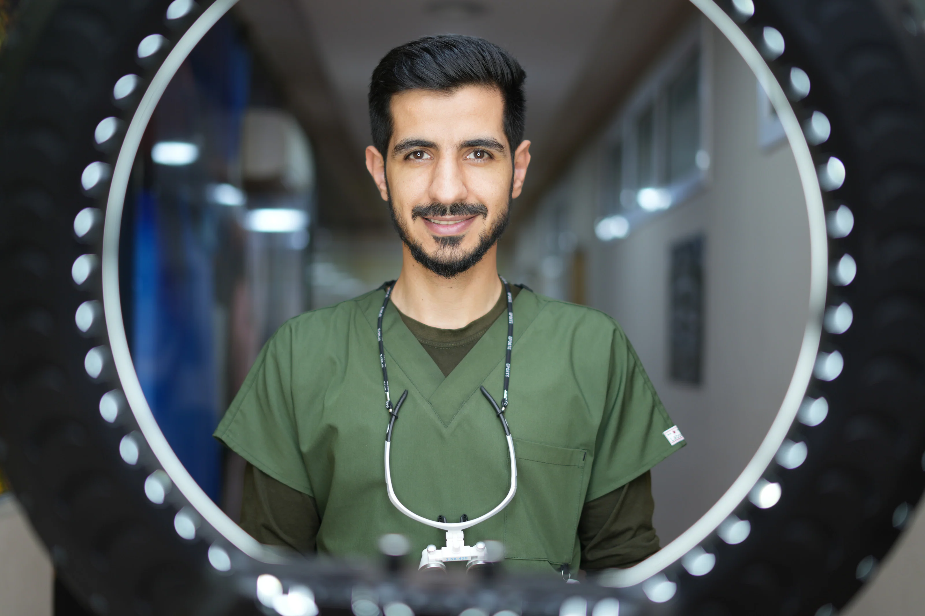 Portrait of Dr. Arash Kiumars in green scrubs, framed by a ring light