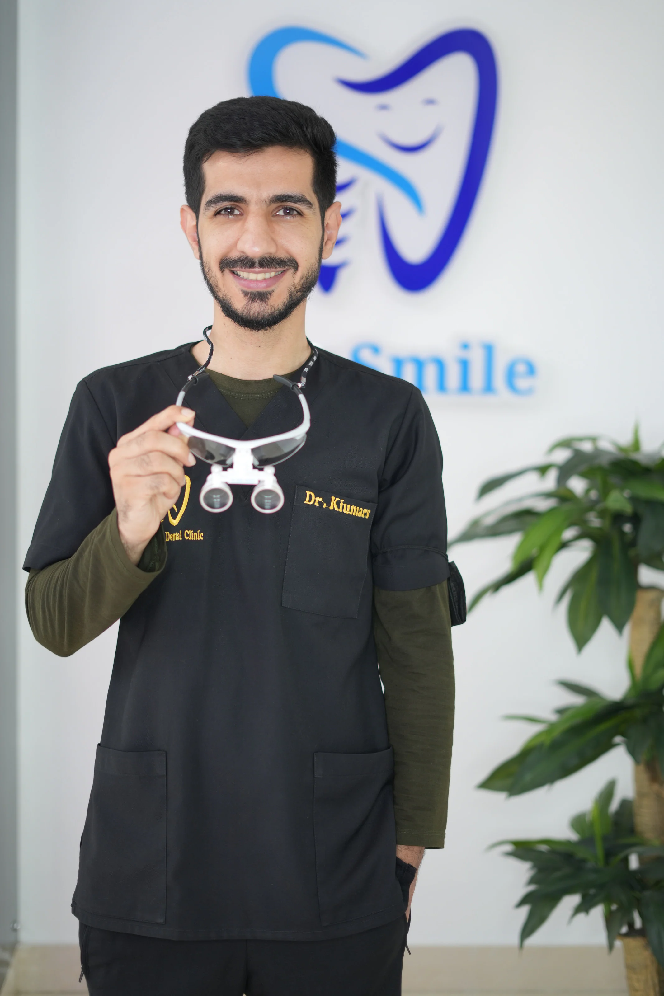 Dr. Arash Kiumars holding dental loupes in front of the City Smile logo